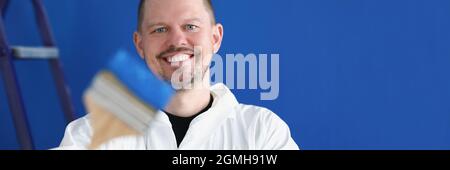 Smiling repairman holding construction brush with blue paint Stock Photo