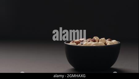 roasted hazelnuts in black bowl on black background, wide photo Stock Photo