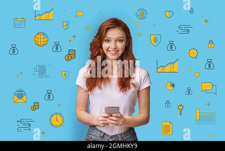 Happy millennial red haired woman using mobile banking application on blue studio background with money related icons Stock Photo