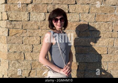 A brunette woman in sunglasses on the background of a stone wall. Stock Photo