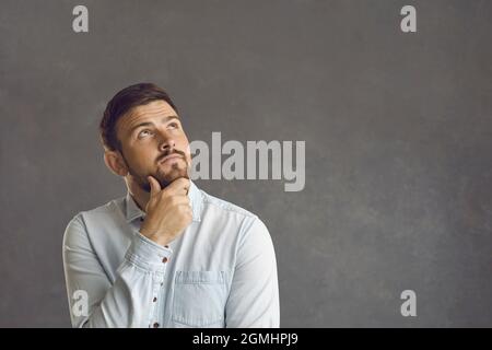 Pensive thoughtful caucasian bearded man touching chin looks up studio shot Stock Photo