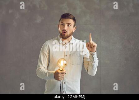 Surprised man thinking and holding glowing lightbulb has bright idea studio shot Stock Photo