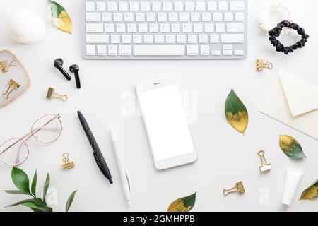 Smartphone mockup with blank screen, computer keyboard and feminine accessories on white table. Flat lay, top view, overhead. Stock Photo
