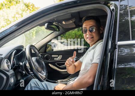a young successful Asian businessman in sunglasses is sitting in an expensive modern car and smiling, looking at the camera. Stock Photo