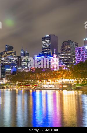 The city of Melbourne, Australia, seen by night from the Yarra River looking across to the city skyline and the 'Arbory Afloat' waterside bar and restaurant.