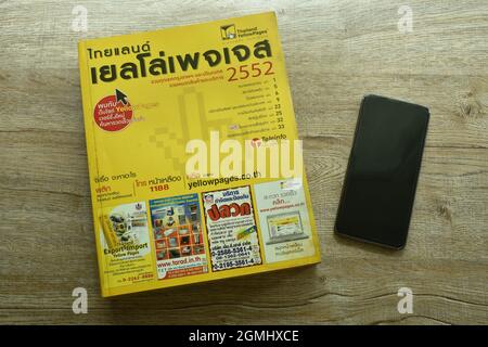 Bangkok Thailand September 19, 2021 : Thailand yellow pages book obsolete method for searching telephone number and address with smartphone on table Stock Photo