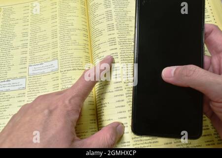 Bangkok Thailand September 19, 2021 : Thailand yellow pages book obsolete method for searching telephone number and address with smartphone on table Stock Photo