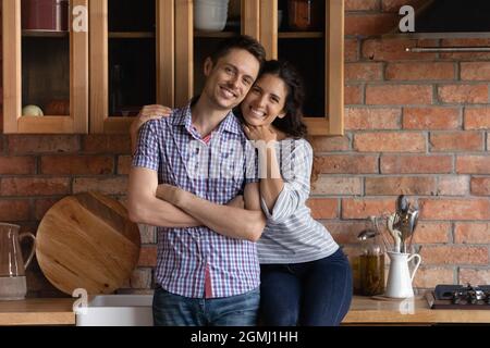 Portrait of smiling bonding millennial hispanic couple posing in kitchen. Stock Photo