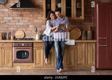 Relaxed smiling young family couple using computer tablet at home. Stock Photo