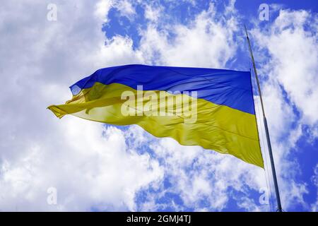 The yellow-blue flag of Ukraine flutters against the blue sky. Ukrainian symbol. A large flag on a flagpole flutters in the wind Stock Photo