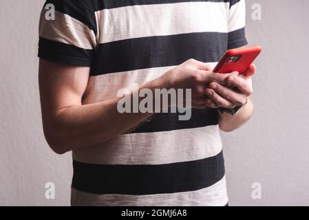 young sport man holding a phone with red case. High quality photo on a gray background Stock Photo