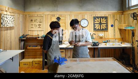 (210919) -- SHIJIAZHUANG, Sept. 19, 2021 (Xinhua) -- Li Zhanlong (R) discusses the design of works with his assistant Li Zhonghua at his studio in Luquan District of Shijiazhuang, north China's Hebei Province, Sept. 14, 2021.  Li Zhanlong is a wooden mechanical installation designer in Shijiazhuang. After graduation, Li once worked as a salesman and ran an online shop. In 2018, Li Zhanlong left his job and went to Tianjin to learn carpentry skills.    The wooden mechanical installation consists of a wooden figure and a mechanism device that can make the installation move. By shaking the handle Stock Photo