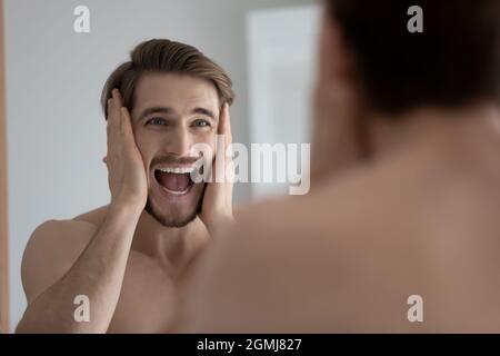 Man looks in mirror shouting feels stressed due skin disorder Stock Photo