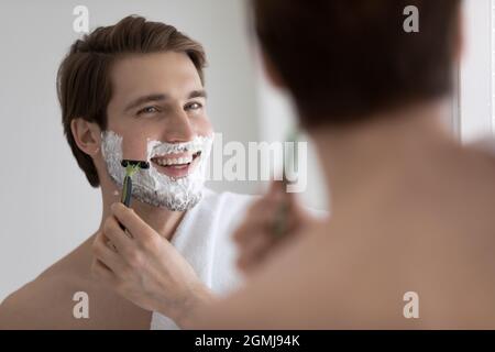 Handsome young man shaving his face and looking in mirror Stock Photo
