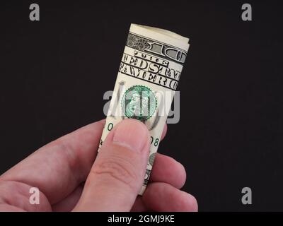 A man holding a folded one hundred dollar bill in his hand. Low key. Close up. Stock Photo