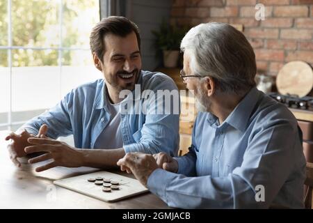Happy young man with mature father playing checkers at home Stock Photo