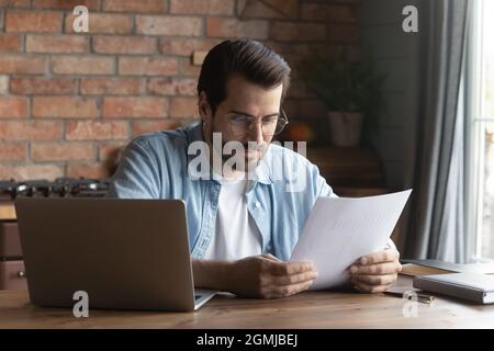 Confident businessman in glasses reading document, sitting at table Stock Photo