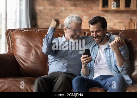 Excited two generations of men celebrating success, using smartphone Stock Photo