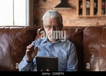 Overjoyed shocked mature man in glasses looking at tablet screen Stock Photo