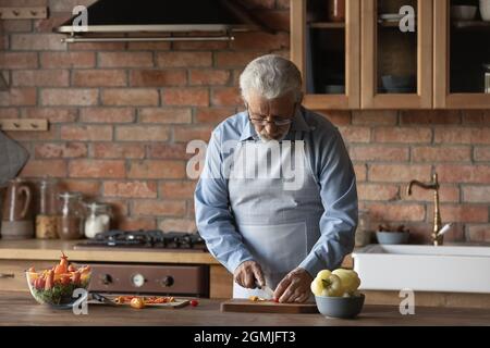 Serious mature man in glasses cutting vegetables, cooking at home Stock Photo