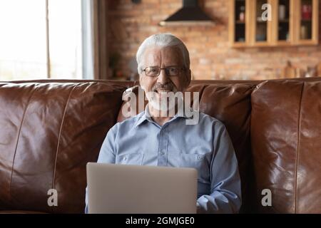 Head shot portrait smiling senior man in glasses using laptop Stock Photo