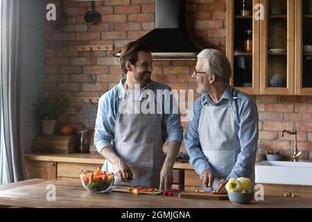 Happy mature father with grownup son cooking salad together Stock Photo