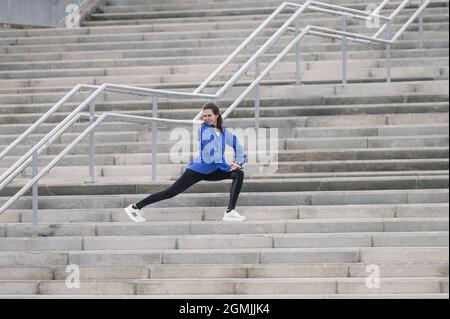 A young Caucasian female jogger doing physical exercises and stretching on a staircase Stock Photo