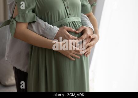 Young male hug pregnant female hold hands on her belly Stock Photo