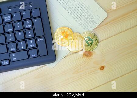 Close up of gold Bitcoin coins on bank passbook with laptop keyboard on wooden table Stock Photo