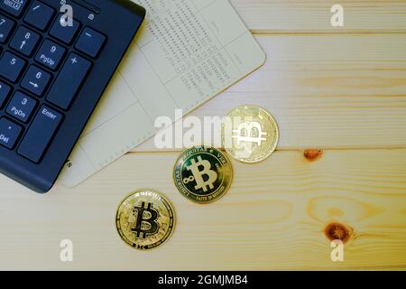 Close up of gold Bitcoin coins on bank passbook with laptop keyboard on wooden table Stock Photo