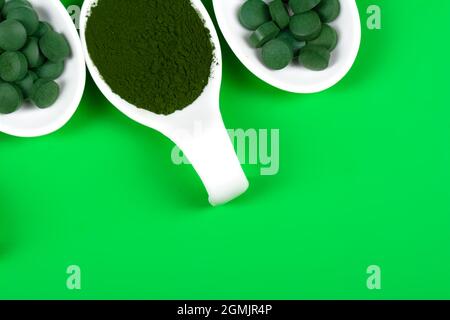 Chlorella or spirulina in the form of tablets and powder on a green background, close up. Stock Photo