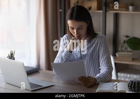 Serious pensive businesswoman reading document, sitting at desk Stock Photo