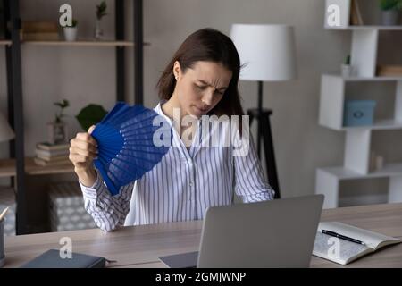 Tired overheated woman waving paper fan, suffering from heat Stock Photo