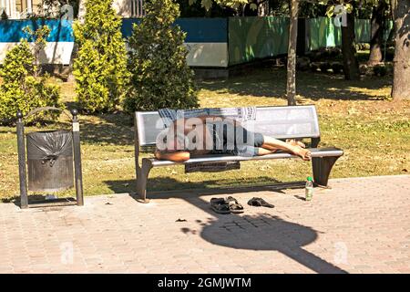 Dnepropetrovsk, UKRAINE - 09.13.2021: A homeless beggar sleeps on a park bench. Social problem. Beggars - unemployed, refugees, emigrants. Stock Photo