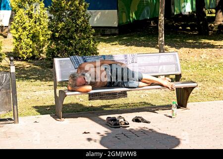 Dnepropetrovsk, UKRAINE - 09.13.2021: A homeless beggar sleeps on a park bench. Social problem. Beggars - unemployed, refugees, emigrants. Stock Photo