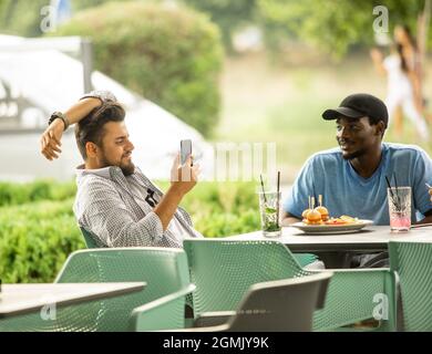 Diverse young friends talking via video call outdoors Stock Photo
