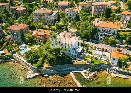 Beautiful villas near the coast of rocky beach in a small town Lovran, Croatia. Arial view of Lungomare sea walkway with transparent water. Stock Photo