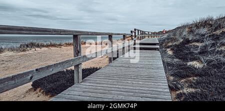 A wooden boardwalk on an elevated grassy coast under a cloudy sky Stock Photo