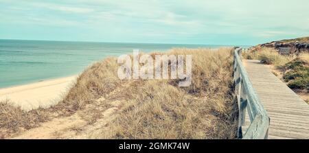 A wooden boardwalk on an elevated grassy coast under a cloudy sky Stock Photo
