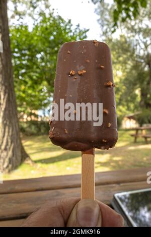 chocolate stick ice cream with almonds held in one hand as a break from teleworking on a garden table Stock Photo
