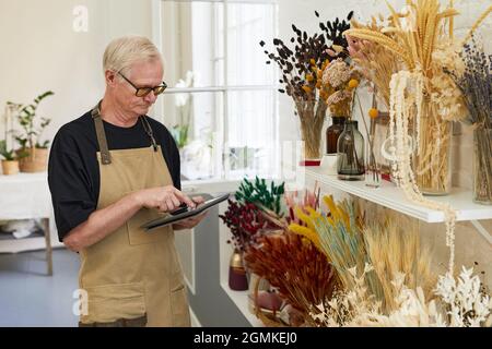 Portrait of modern senior man doing stock inventory while working in florists shop, copy space Stock Photo