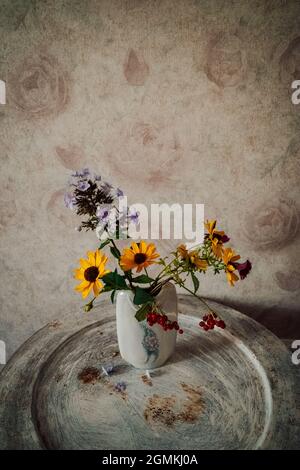 A vertical shot of a clay plate and a vase full of colorful flowers in it Stock Photo