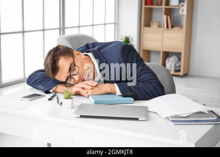 Young man falling asleep during work in office Stock Photo