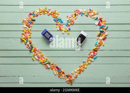 Heart made of pills and pulse oximeters on color wooden background Stock Photo