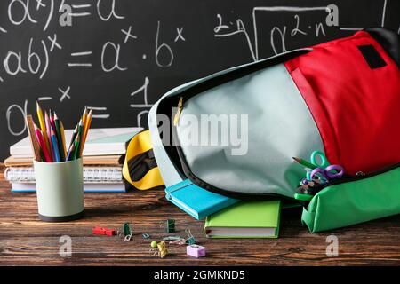 School backpack with stationery on wooden table in classroom Stock Photo