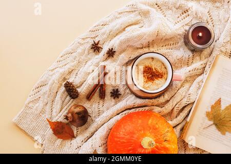 A cup of pumpkin latte on the table with book, candle, yellow leaves and spices on a knitted sweater background. Autumn concept, top view, flat lay Stock Photo