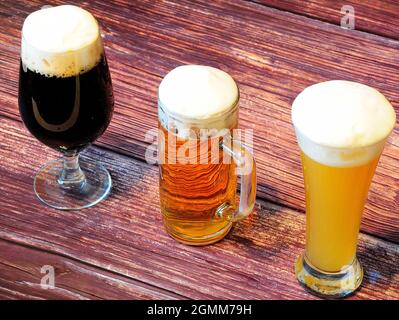 Beer, wheat, light and dark, in different glasses, stand in a row on a dark wooden table. Close-up. Stock Photo