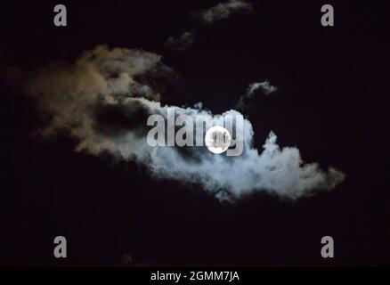 A full moon illuminates passing clouds in a night sky. Stock Photo