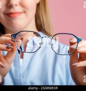 Eyeglasses in hands. Blue fashionable metal glasses for vision in hands of smiling young woman. Eye health Checking, vision correction via Eyeglasses Stock Photo