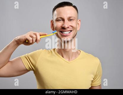 Portrait of happy friendly smiling adult man in yellow t-shirt with toothbrush demonstrates his healthy white teeth Stock Photo